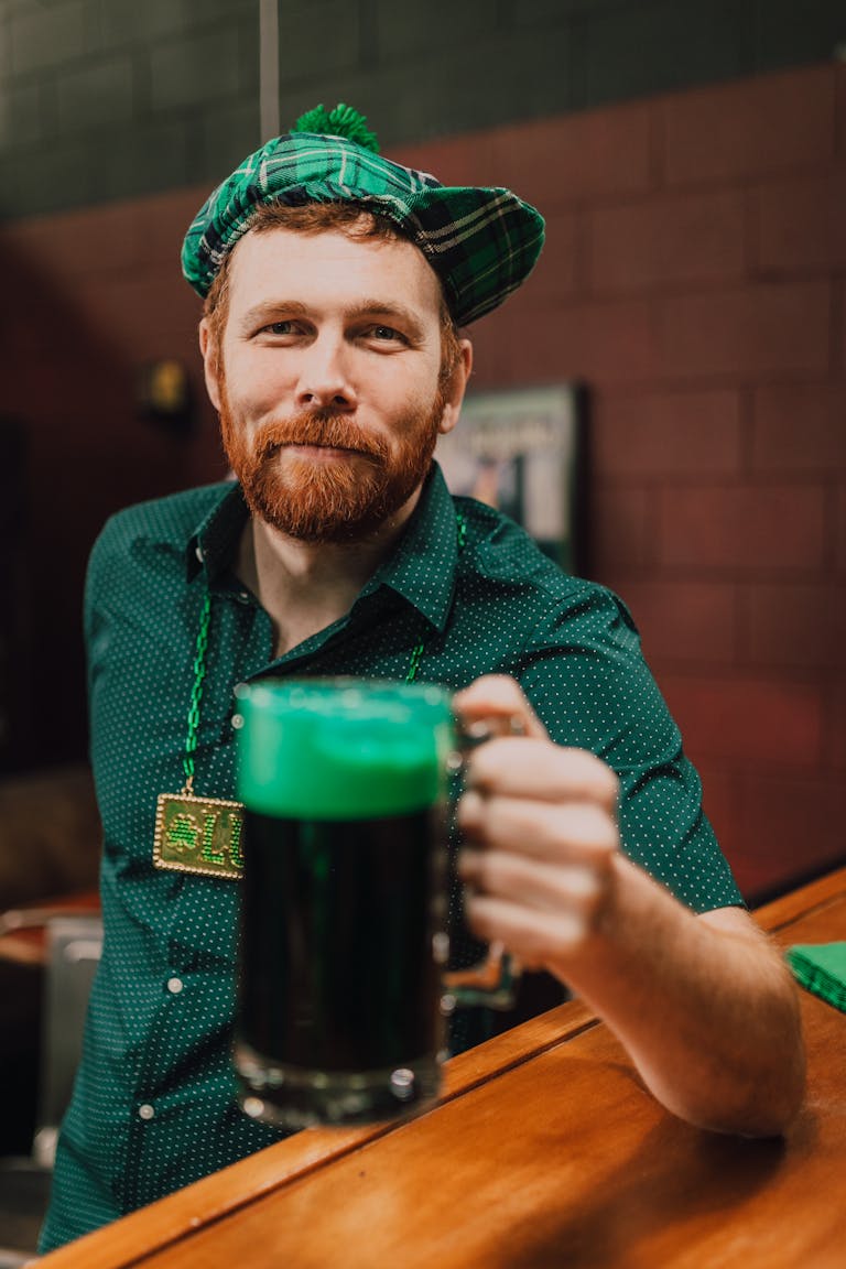 Adult man in Irish attire holding green beer at St. Patrick's Day party.